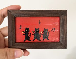 赤い背景に黒猫が3匹楽しそうに踊っているポップで明るい雰囲気のテクスチャーアート。Yuka Mitsufuji作品。